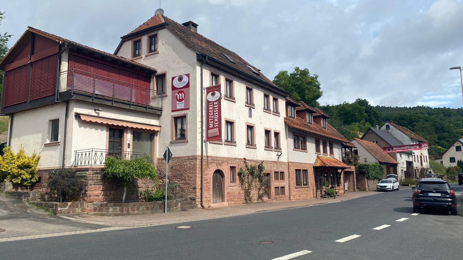 Foto der Metzgerei Schüssler Filiale in Hobbach. Hausansicht mit davor liegender Straße, freundlicher blauer Himmel.