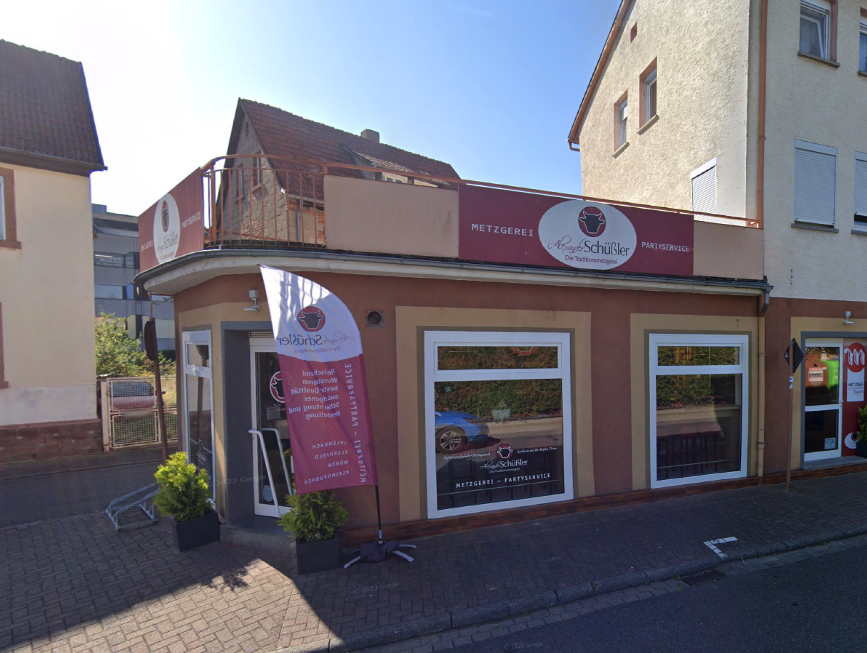 Foto der Metzgerei Schüssler Filiale in Kleinheubach. Hausansicht mit davor liegender Straße, stahlend blauer Himmel.