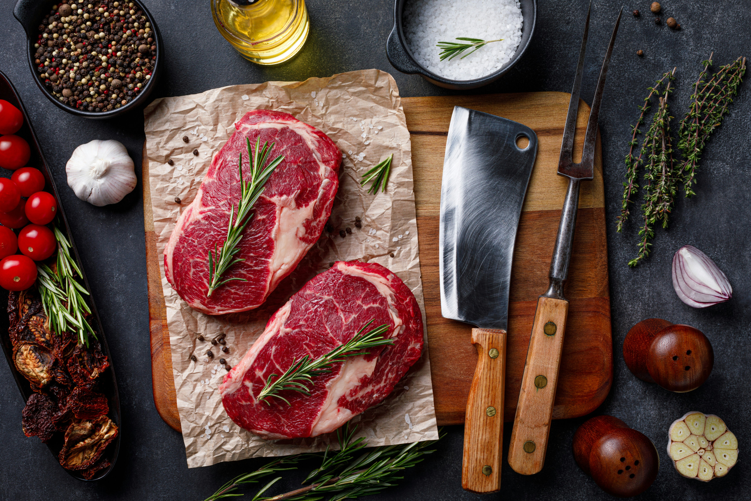 Zwei rohe Steaks mit Rosmarin, daneben Messer und frische Zutaten.