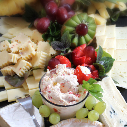 Käse-Obst-Platte mit Trauben, Erdbeeren, Kiwi und cremigem Dip.