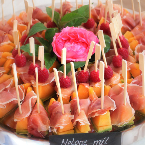 Melonenspieße mit Rohschinken und Himbeeren auf einer Catering-Platte.