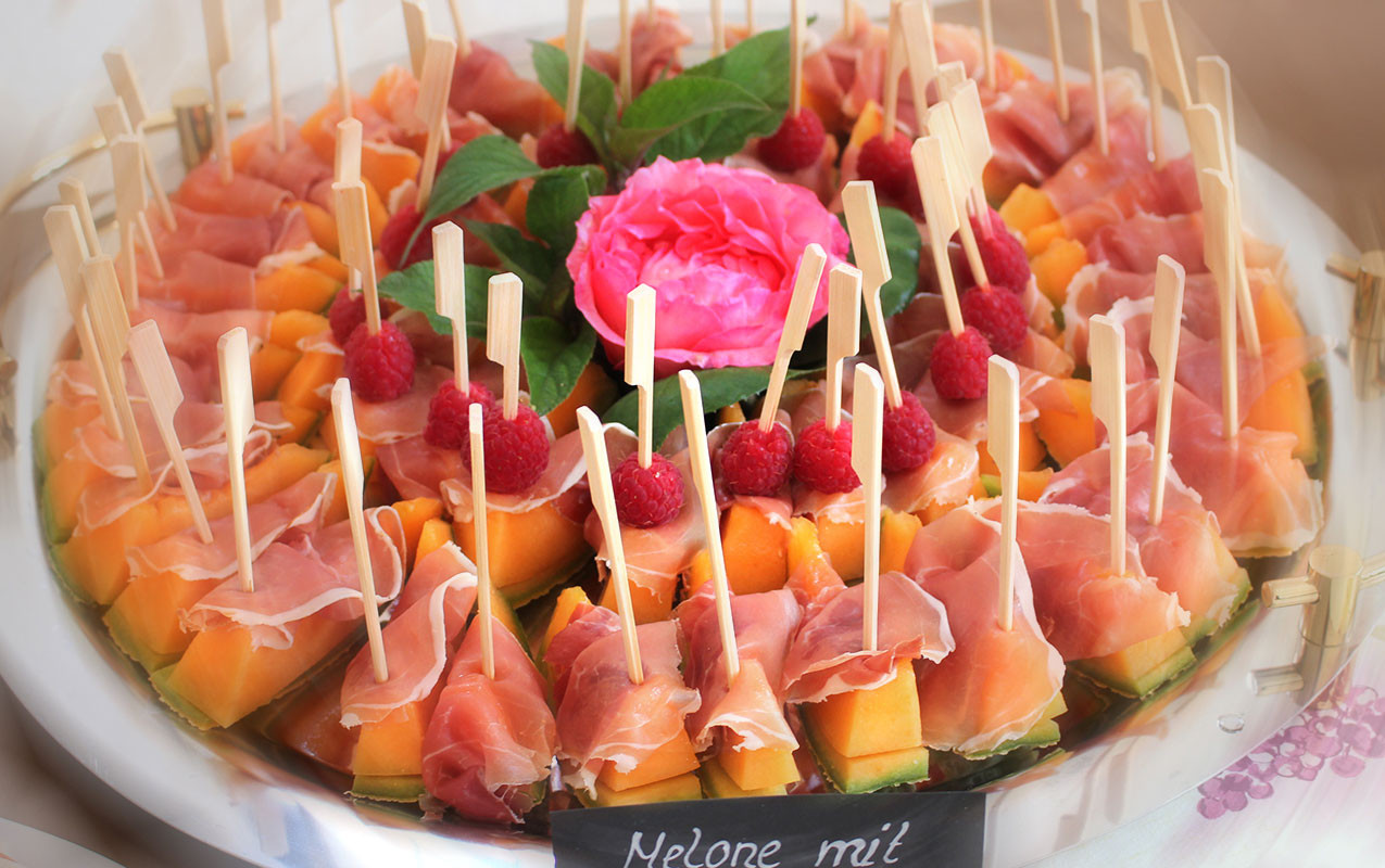 Melonenspieße mit Rohschinken und Himbeeren auf einer Catering-Platte.